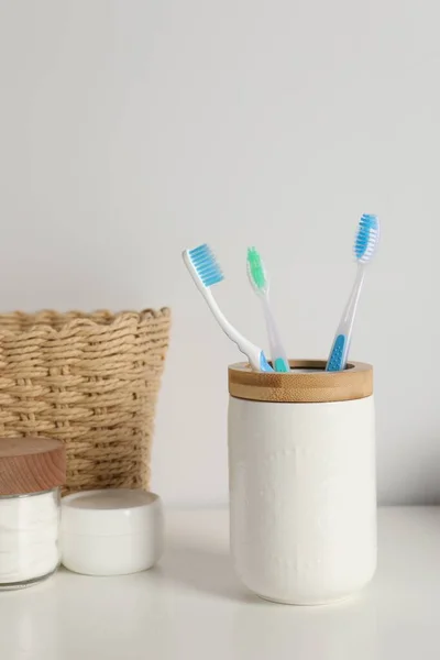 Plastic toothbrushes in holder and cosmetic products on white countertop