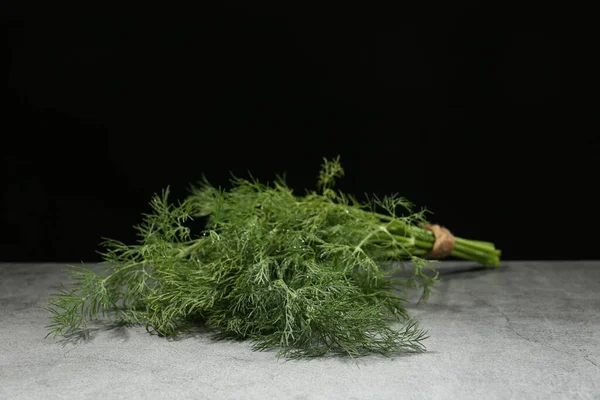 Açık gri masada siyah arka planda su damlaları olan bir demet taze dereotu.