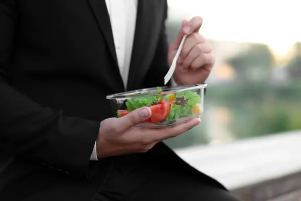 Businessman eating from lunch box outdoors, closeup