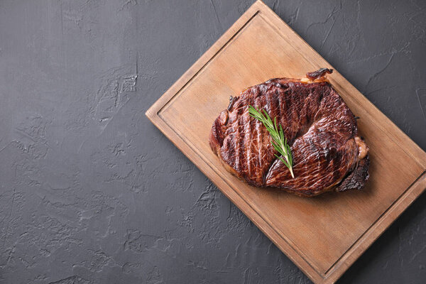 Wooden board with delicious fried beef meat and rosemary on grey textured table, top view. Space for text