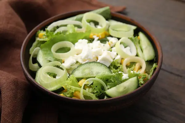 Bowl of tasty salad with leek and cheese on wooden table, closeup
