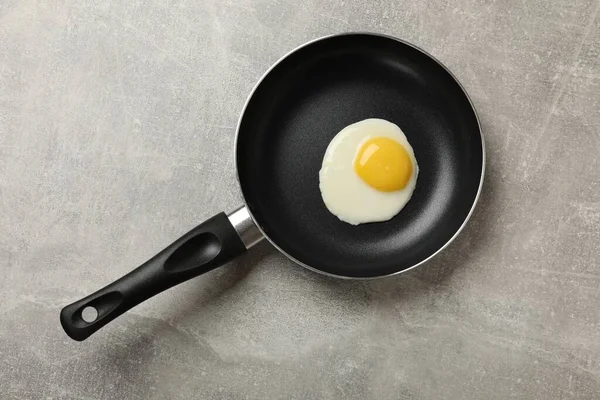 Delicious fried egg in frying pan on grey table, top view