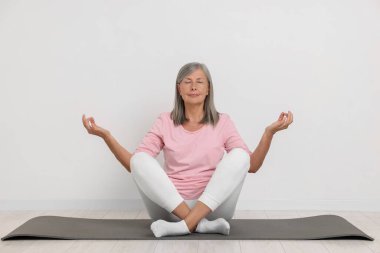 Yaşlı kadın beyaz duvarın yanında yoga yapıyor.
