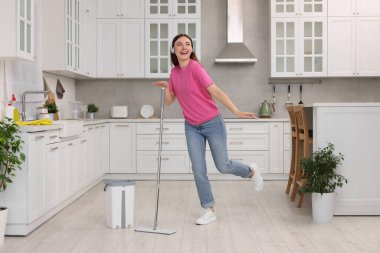 Temizliğin tadını çıkarıyorum. Kulaklıklı mutlu kadın mutfakta paspasla dans ediyor.