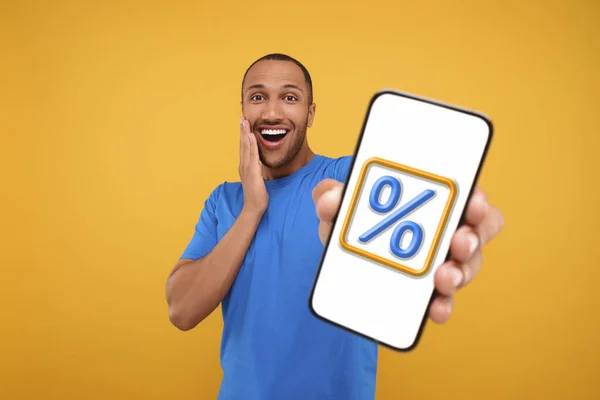 Discount, offer, sale. Emotional man showing mobile phone with percent sign on screen, orange background