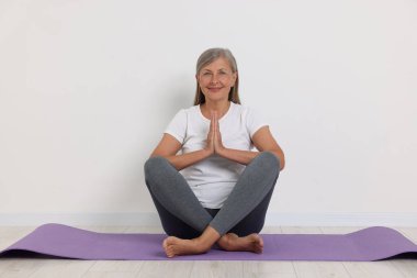 Beyaz duvarın yanında yoga yapan mutlu son sınıf kadını.