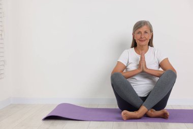 Beyaz duvarın yanındaki minderde yoga yapan mutlu bir son sınıf öğrencisi. Metin için boşluk