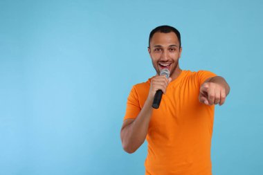 Açık mavi arka planda mikrofonlu yakışıklı adam şarkı söylüyor, mesaj için yer var.