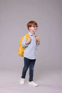 Gri arka planda sırt çantası olan mutlu okul çocuğu.