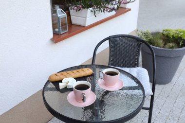 Bardaklar dolusu kahve, ekmek ve peynir cam masada. Açık terasta dinlenme yeri