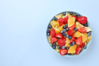 Açık mavi arka planda, kasede lezzetli meyve salatası, üst manzara. Metin için boşluk