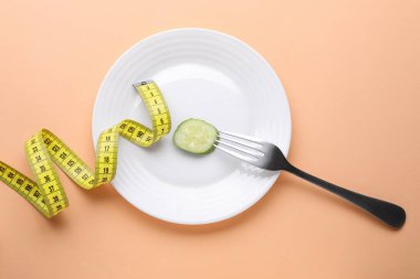 Salatalık dilimli, çatallı ve soluk turuncu arka planda mezuralı bir tabak. Diyet kavramı