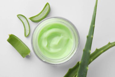 Kozmetik krem kavanozu ve beyaz arka planda aloe yaprakları, düz uzanma