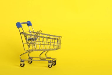 Sarı arka planda küçük metal alışveriş arabası. Metin için boşluk