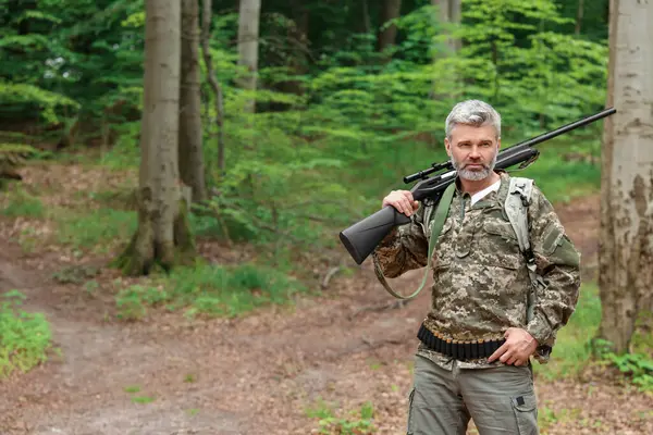 Man with hunting rifle wearing camouflage in forest. Space for text