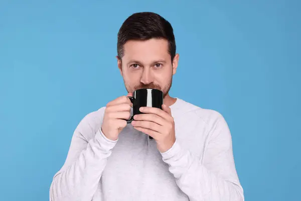 Portrait of man drinking from black mug on light blue background