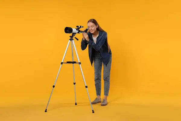 Young astronomer looking at stars through telescope on orange background