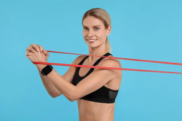 Woman exercising with elastic resistance band on light blue background