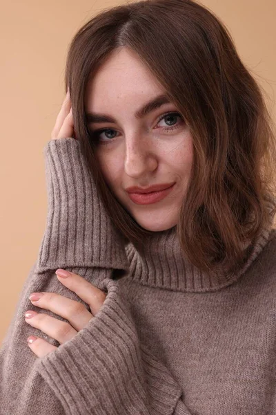 茶色の背景に暖かいセーターで美しい若い女性の肖像画 — ストック写真