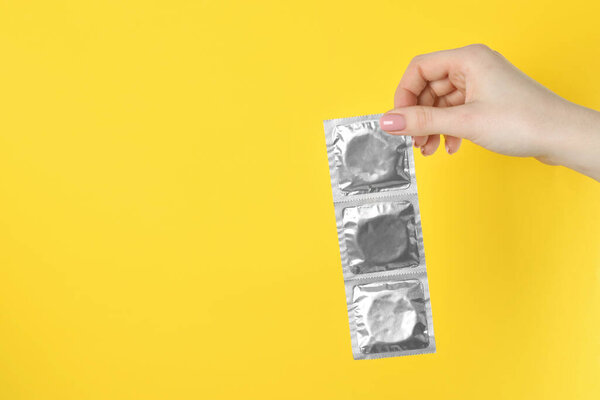 Женщина держит презервативы на жёлтом фоне, крупным планом. Пространство для текста