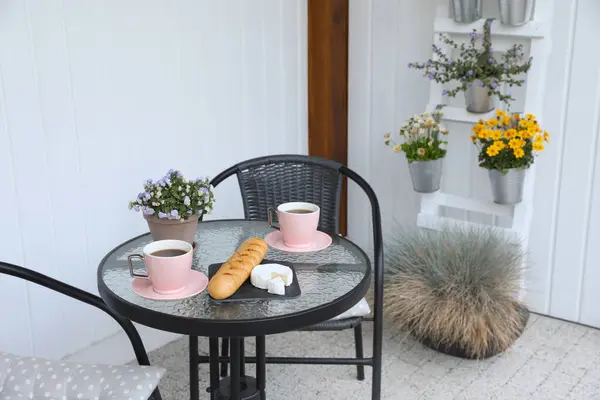 Cups of coffee, potted plant, bread and cheese on glass table. Relaxing place at outdoor terrace