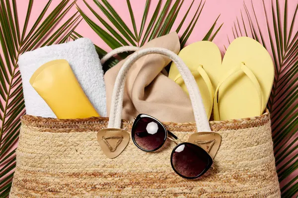 Flat lay composition with wicker bag, palm leaves and other beach accessories on pink background