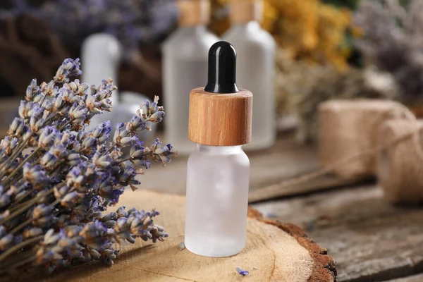 Bottle of essential oil and dry lavender flowers on wooden table, closeup. Medicinal herbs