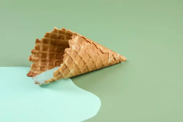 Melted ice cream and wafer cone on green background, closeup. Space for text