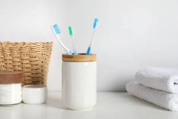 Plastic toothbrushes in holder, towels and cosmetic products on white countertop