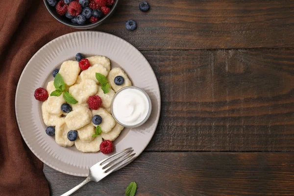 Plate of tasty lazy dumplings with berries, sour cream and mint leaves on wooden table, flat lay. Space for text