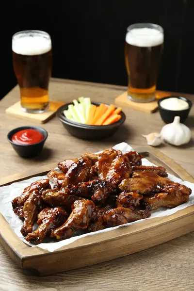 Tasty chicken wings, sauces, vegetable sticks and glasses of beer on wooden table. Delicious snacks