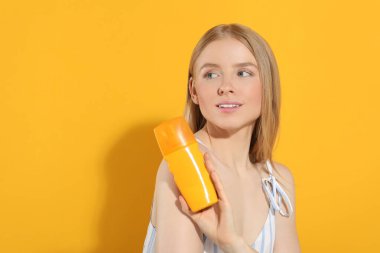 Turuncu arka planda güneş kremi tutan güzel genç bir kadın. Mesaj için yer var.