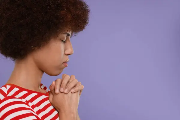 Woman with clasped hands praying to God on purple background. Space for text