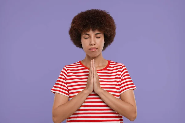 Woman with clasped hands praying to God on purple background
