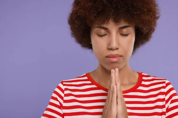 Woman with clasped hands praying to God on purple background. Space for text