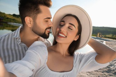 Romantik bir randevu. Güneşli bir günde gölün yanında selfie çeken güzel bir çift.