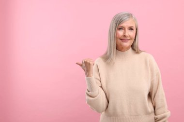 Güzel orta yaşlı kadın portresi pembe arka planda bir şeyi işaret ediyor, mesaj için boşluk.