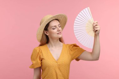 Pembe arka planda serinlemek için sarı yelpaze sallayan güzel bir kadın.