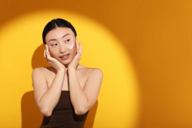 Güneş ışığı altında güzel bir genç kadın. Yüzünde turuncu arka planda güneş kremi var. Mesaj için yer var.