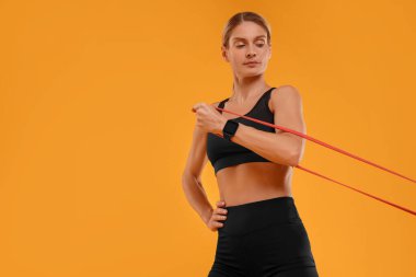 Turuncu arka planda elastik direnç bandıyla egzersiz yapan kadın, düşük açılı görüş. Metin için boşluk