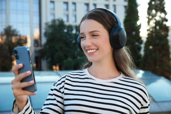Smiling woman in headphones using smartphone on city street