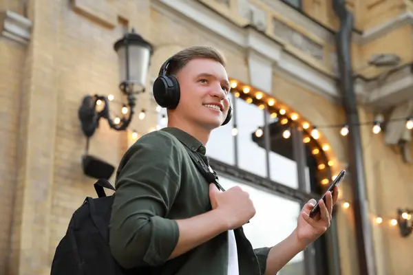 Smiling man in headphones and smartphone outdoors, low angle view