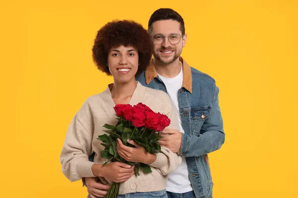 International dating. Happy couple with bouquet of roses on orange background