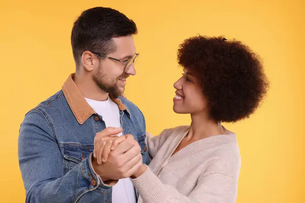 International dating. Lovely couple dancing on orange background