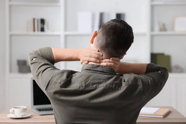 Man massaging stiff neck in office, back view