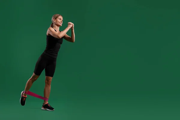 Smiling woman exercising with elastic resistance band on green background, low angle view. Space for text