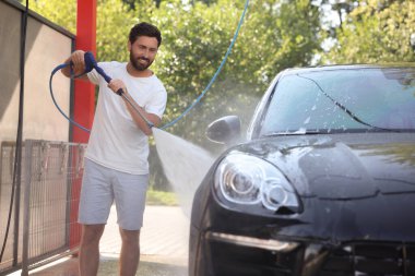 Dışarıdaki oto yıkamada yüksek basınçlı su jetiyle araba yıkayan mutlu bir adam.