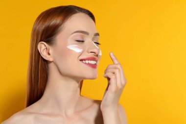 Yüzünde güneş kremi olan güzel genç bir kadın turuncu arka planda, mesaj için yer var.