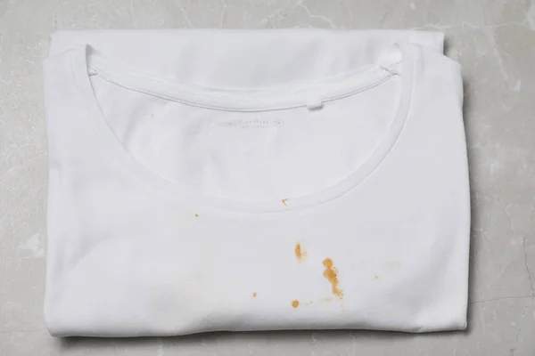 Dirty t-shirt with stains of sauce on light grey marble table, top view