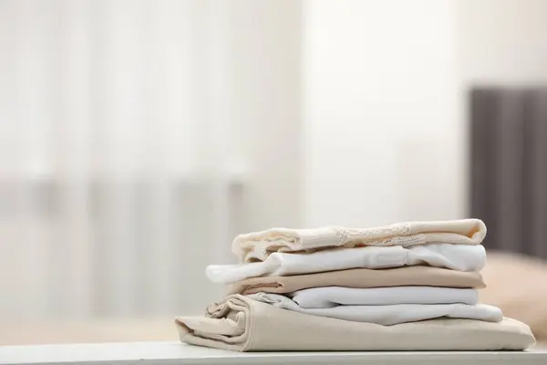 Stack of different folded clothes on white table indoors, closeup. Space for text